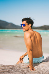 Male model wearing sunglasses and fitness body on the beach posing