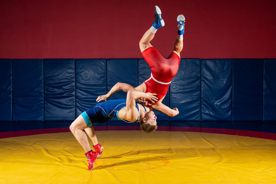 Two  strong men in blue and red wrestling tights are wrestlng and making a suplex wrestling on a yellow wrestling carpet in the gym. Wrestlers doing grapple.