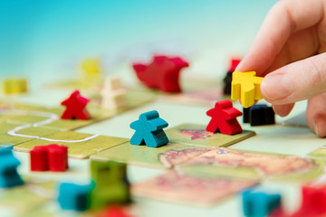 Colorful board game figures on the field, hobby. Meeple in hand
