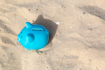 Fototapeta na wymiar Blue piggy bank pig on warm fine sea sand, savings on vacation. The concept of accumulating money for a summer vacation.