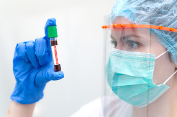 Woman in face mask and face shield checking test tube for testing blood for coronavirus. Concept...