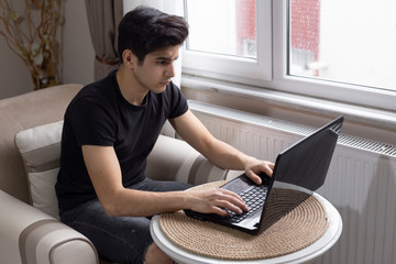 Teenage male student is studying at home, listening to music and surfing the internet.