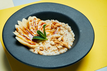 A delicious and healthy breakfast - oatmeal in milk with bananas, nuts and candied fruits in black bowl isolated colored background. Diet food