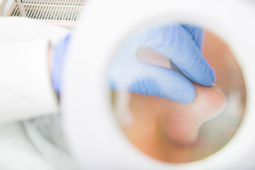 Beautician examines pores with magnifying mirror in medical office