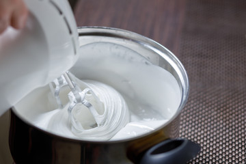 Woman whisking with mixer eggs whites with sugar