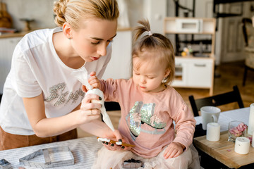 Beautiful young mom and her cute little daughter making cookies in kitchen