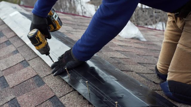 Builder is attaching ridge on the roof using a screw gun. Frame house under construction