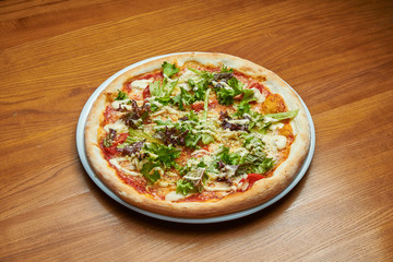 Appetizing baked Italian pizza with cream sauce, lettuce, chicken and parmesan on a white plate on a wooden background. Pizza caesar