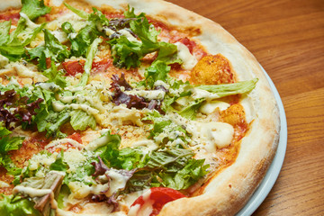 Appetizing baked Italian pizza with cream sauce, lettuce, chicken and parmesan on a white plate on a wooden background. Pizza caesar