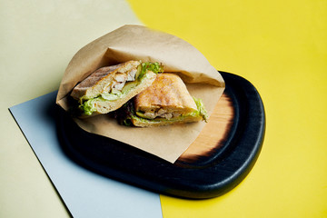 Sandwich in a ciabatta bun with ham, tomatoes, pickled cucumber cheese and lettuce on a wooden tray. Close up. Tasty fast food