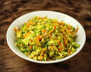 green sweet spring cabbage salad with carrots and parsley in a white bowl