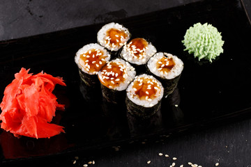 Set of baked sushi rolls with wasabi and ginger on a black background.