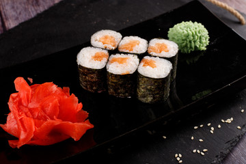Set of baked sushi rolls with wasabi and ginger on a black background.