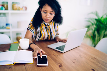 Female freelancer browsing smartphone and laptop at home