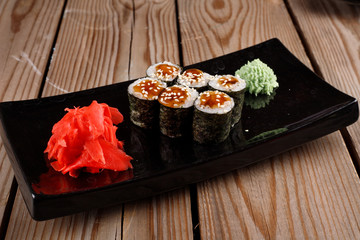 Set of baked sushi rolls with wasabi and ginger on a black background.
