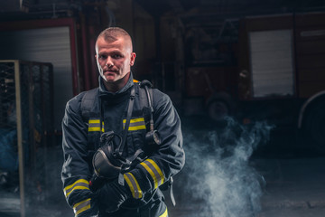 Portrait of a fireman wearing firefighter turnouts and helmet. Dark background with smoke and blue...
