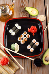 Set of baked sushi rolls with wasabi and ginger on a black background.