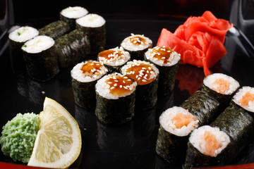 Set of baked sushi rolls with wasabi and ginger on a black background.