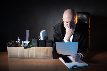 The businessman studies the document on a dark background. Busin