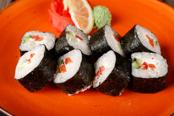 A set of baked sushi rolls with wasabi and ginger on an orange plate background.