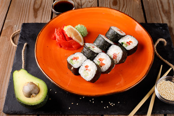 A set of baked sushi rolls with wasabi and ginger on an orange plate background.