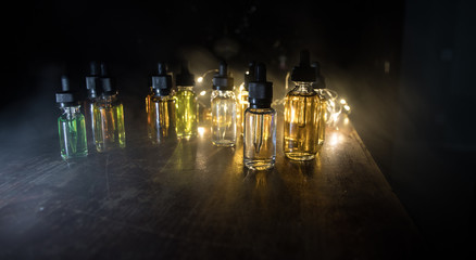 Smoke clouds and vape liquid bottles on dark background. Light effects. Useful as background or...