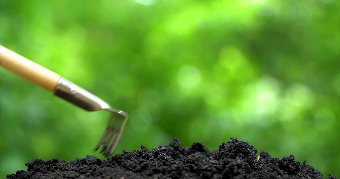 Human hand to rake the ground by rake and waterering by from vintage pulverizer. Closeup side view on green background.