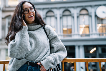 Cheerful woman standing on street and talking on cellphone