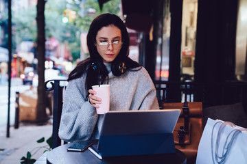Fototapeta premium Attractive freelance woman having drink while browsing tablet in street cafe