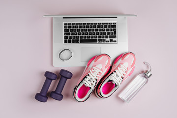 Laptop with fitness sports equipment and sneakers on a pink background.  Home online workout. Top...