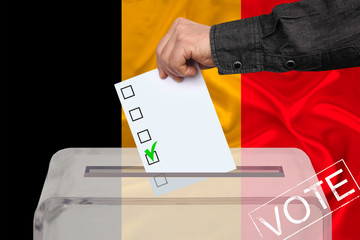 male voter drops a ballot in a transparent ballot box against the background of the national flag...