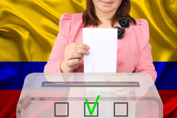 female voter drops a ballot in a transparent ballot box against the backdrop of the Colombia...
