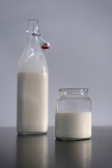 A glass filled with milk and a bottle stand on a table.