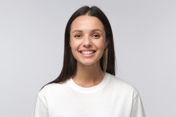 Young happy smiling brown hair woman dressed in white blank T-shirt, feeling positive and looking...