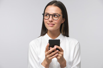 Business girl in glasses looking to left side typing messages on smartphone, looking interested and...