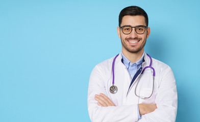 Fototapeta premium Banner of smiling young male doctor wearing white coat and round eyeglasses, isolated on blue background