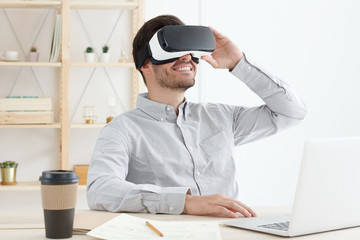 Young business guy experiencing opportunities of virtual reality, discovering VR game setting and enjoying free time in his office, smiling positively