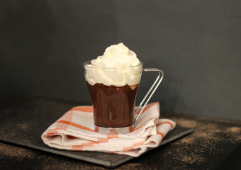 Glass of hot chocolate with whipped cream on dark background