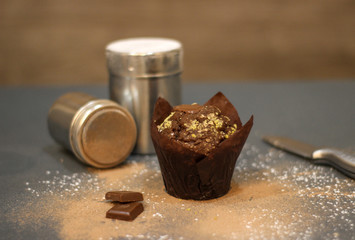Chocolate muffin on dark background with cocoa powder and chocolate bar, knife and dispensers