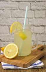Lemonade in a glass mug and a slice of lemon in a wooden board and white and blue cloth vertical