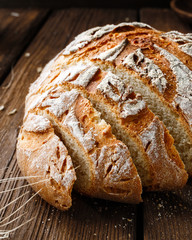 Круглый хлеб из пшеничной муки нарезанный кусками на льняной салфетке лежит на деревянном столе, рядом лежит колосок