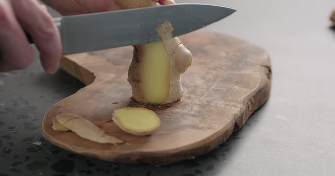 Slow motion man hands peeling fresh ginger root with knife on olive wood board