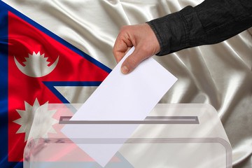 male voter drops a ballot in a transparent ballot box on the background of the Nepal national flag,...