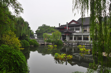Fototapeta na wymiar A Chinese building on the shores of West Lake in Hangzhou. The trees and the house are reflected in the water.