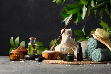 Spa and bath concepts. A scrub of ground coffee and oranges, oil for body and cotton pouches with herbs for massage, sea stones, towels and other Spa accessories on dark table.