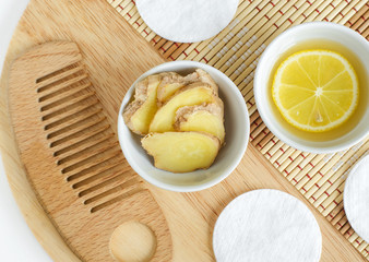 Ginger slices in the small white bowl, wooden hair comb and lemon juice and slice. Natural homemade hair treatment and zero waste concept. Top view, copy space