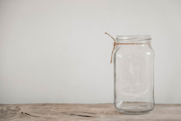 Glass transparent jar on wooden table on white wall background. Copy, empty space for text
