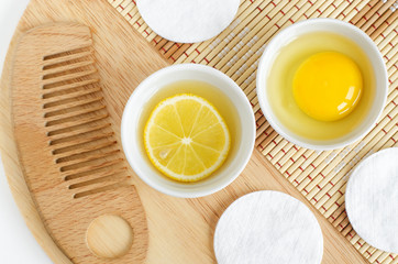 Lemon juice with lemon slice, raw egg in the small white bowls and wooden hair brush. Natural homemade hair treatment and zero waste concept. Top view, copy space