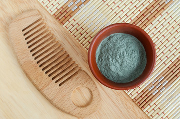 Green (blue) bentonite clay powder in the bowl and wooden hair brush. Clay texture close up. Diy facial or hair mask and body wrap recipe. Natural beauty treatment and spa. Top view, copy space