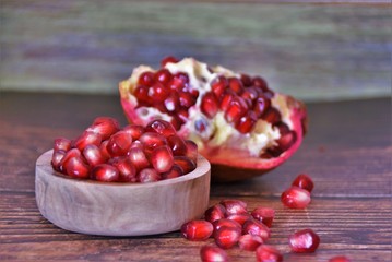 red pomegranate seeds in a wooden bowl and on a wooden table